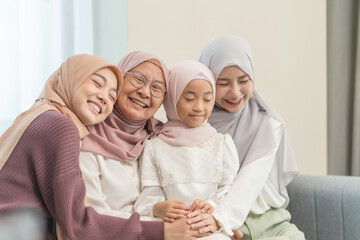 portrait of happy three different generations female muslim family meeting at home,sitting on couch in living room,hugging with love, smile,enjoy holiday time together
