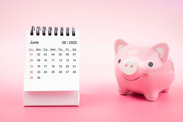 Desk calendar for June 2025 and pink piggy bank on pink background.