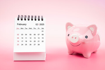 Desk calendar for February 2025 and pink piggy bank on pink background.