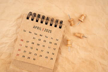 April 2025 desk calendar with wooden thumbtack on brown crumpled paper background.