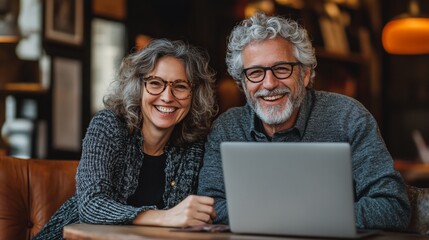 Happy senior couple smiling at the camera while using a laptop in a cafe.
