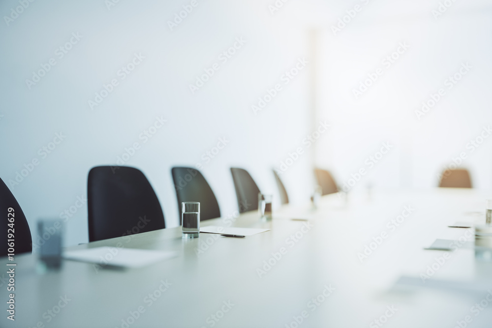 Poster light conference table with glasses of water and clean paper sheets surrounded by dark chairs in mee