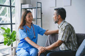 Fototapeta premium Young nurse holding senior patient's hands, comforting him during a home visit, providing medical and emotional support