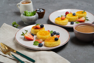 Fried syrniki with fresh berries on a light plate on a dark table
