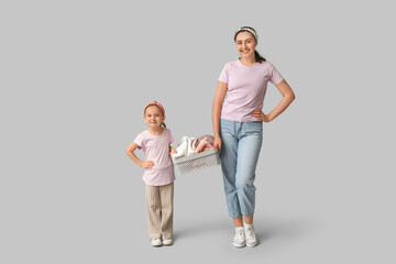 Happy mother and her daughter with clean towels in basin on grey background