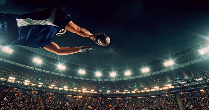 This video captures a dramatic moment in an American football game as a player in a blue jersey dives mid-air to catch the ball. The bright stadium lights and cheering crowd amplify the intensity and 
