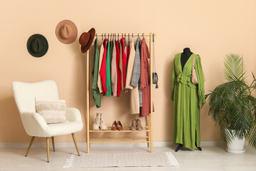 Rack with clothes, armchair and mannequin near beige wall in dressing room