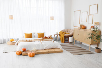 Interior of light bedroom with pumpkins, armchair and commode