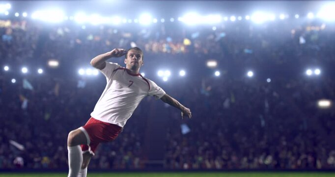 Football player, wearing red and white uniform, kicks the ball in a jump, in slow motion on the professional football stadium with animated crowd.