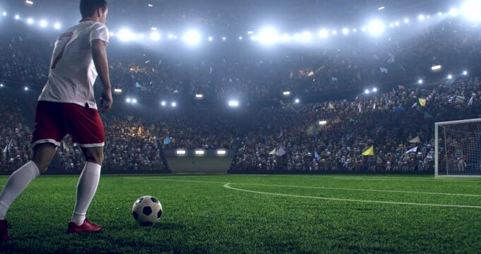 Football player is dribbling the ball down the field and kicks the ball towards the goal while other players trying to interfere. Professional stadium with animated crowd.