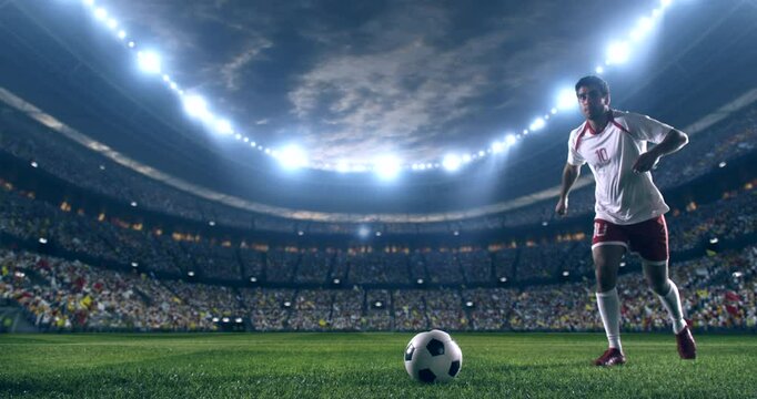 Football player wearing red and white uniform, kicking a ball in slow motion towards the camera on a professional stadium at night.
