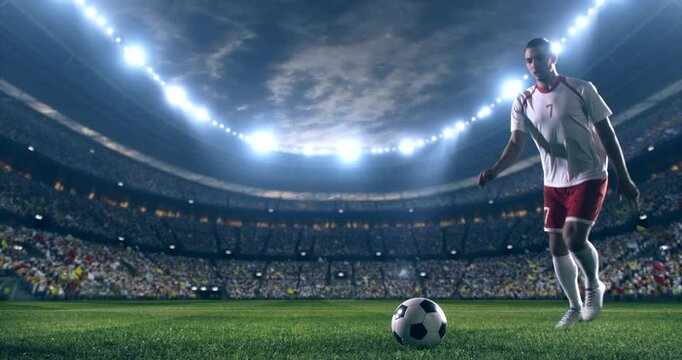 Football player wearing red and white uniform, kicking a ball in slow motion towards the camera on a professional stadium at night.