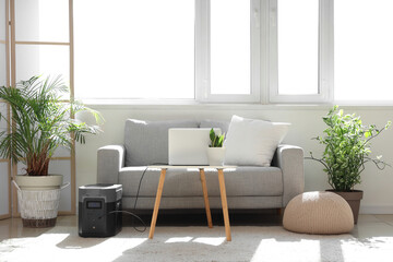 Interior of light living room with sofa, laptop on table and portable power station