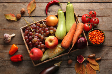 Wicker box with different fresh vegetables, fruits and autumn leaves on wooden background. Harvest festival