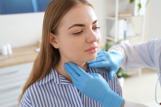 Male endocrinologist examining woman's thyroid gland in clinic, closeup