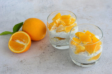 two glasses of yogurt with chia seeds next to two oranges