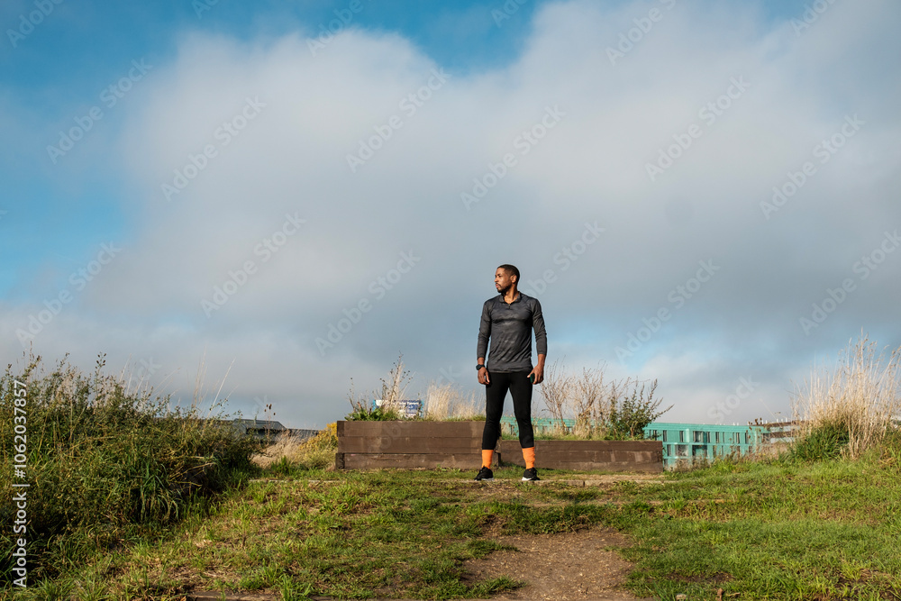 Wall mural confident black athlete standing on hilltop overlooking cityscape