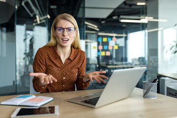 Mature business woman expressing frustration during video call in office. Wearing glasses, using...