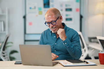 Happy mature businessman feeling euphoric about successful project, celebrating achievement at...