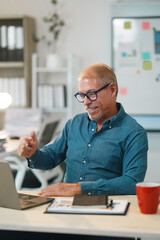 Happy businessman showing thumbs up gesture during a video conference on his laptop, enjoying a successful online meeting