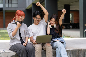 Group of cheerful students expressing joy and achievement while using a laptop on campus