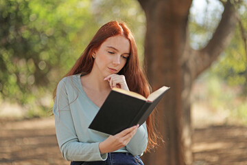 A woman in a park is reading a book intently