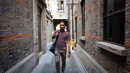 Asian man with sling bag walking in a rush through a narrow street in China.