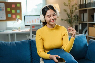 Obraz premium Young asia businesswoman using smartphone and listening music with headphone working on sofa in living room at house