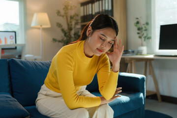 Stressed asian freelancer woman suffering from headache while working from home sitting on sofa