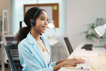 Friendly female support employee managing helpline service, typing on keyboard and talking with...