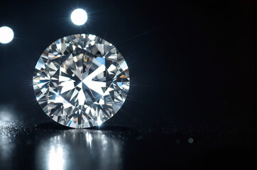 A stunning diamond sits illuminated under bright lights, casting reflections and emphasizing its sharp facets and clarity on a dark surface