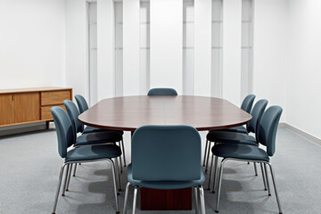 The image shows a modern, minimalist conference room with a dark wood table, eight armless chairs, light grey carpet, wooden sideboard, white walls, and modern architectural style.