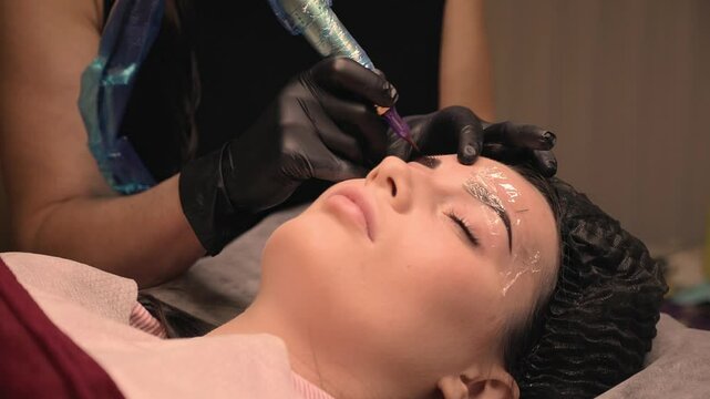 Cosmetologist applies permanent eyebrow tattoo to a woman