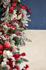 Christmas garland with pine needles, white branches and red decorations on a blue background