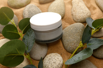 Cosmetic cream in a glass container on stones with eucalyptus branches.