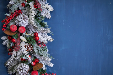 Christmas garland with pine needles, white branches and red decorations on a blue background