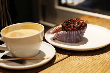 Cozy coffee shop scene with a cappuccino and chocolate muffin on a wooden table by a window in a coffee shop. Selective focus