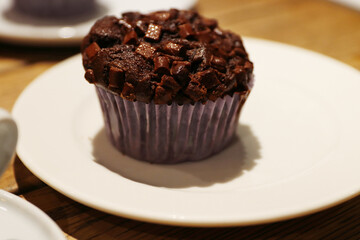 Chocolate muffin on the white plate.  Homemade Cupcake with chocolate chips on the wooden table in café. Delicious Brownie cake. Cozy atmosphere. Closeup. Side view