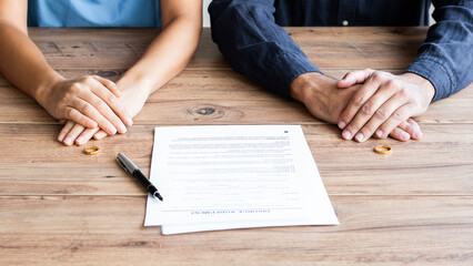 Human hand signing divorce contract, close-up. Wedding rings with marriage contract and judge gavel...