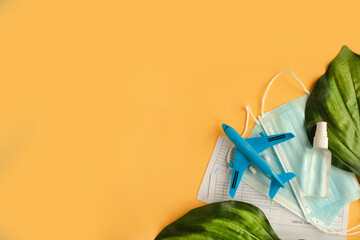 Toy airplane, hand sanitizer and face medical mask on yellow background. Travel during the...