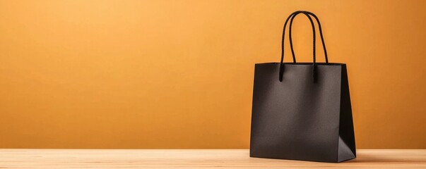 Black shopping bag on a wooden table against an orange wall.