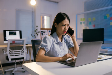 Stressed young businesswoman works late in her dimly lit office, managing tasks and deadlines on...