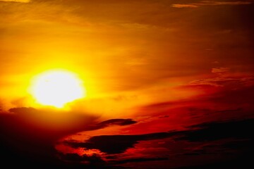 Fototapeta premium This is a beautiful sunset or sunrise photo with bright orange, yellow, and red as the main colors in the sky. The sun is partially obscured by clouds, which makes the sky look brighter and warmer.