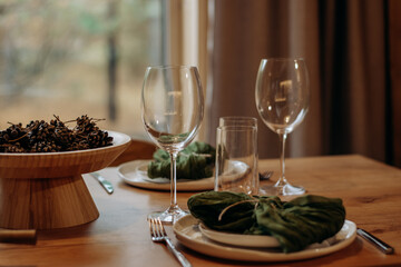 Christmas table setting featuring a fir branches, a cones, a green napkins against the background of a wooden table.