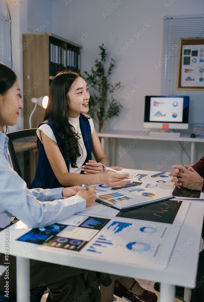 Poster businesswomen are sitting at a table, discussing business performance and pointing at charts and gra