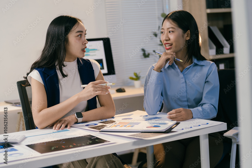 Poster two young businesswomen are sitting at office desk, actively discussing business strategies while an