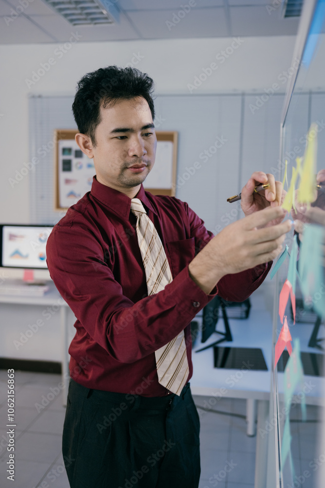 Poster asian businessman writing on sticky notes attached to a glass wall in an office meeting room, develo