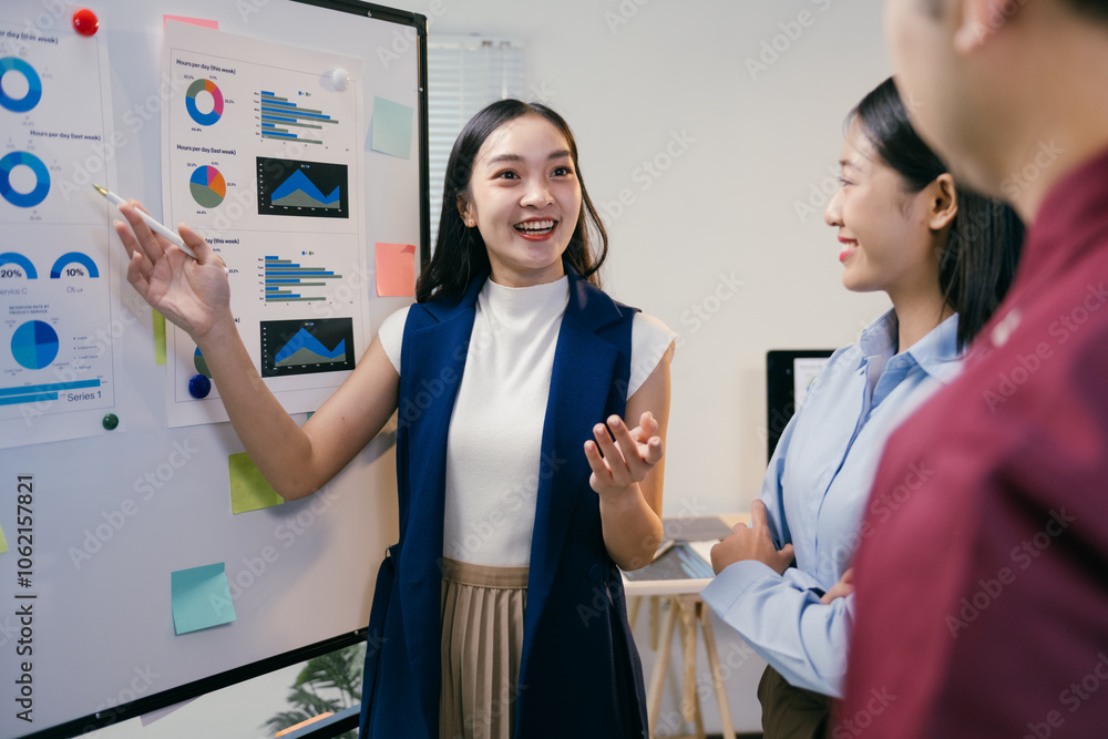 Poster young businesswoman explaining business strategy using charts and graphs on whiteboard to her cowork