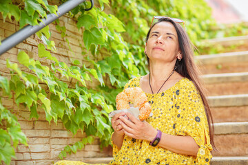 Positive attractive brunette woman in yellow dress sitting on stairs with bagel