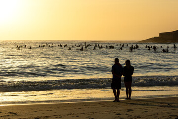 People at the beach and on SUP boards watching the sunrise at Copacabana Beach in Rio de Janeiro in...